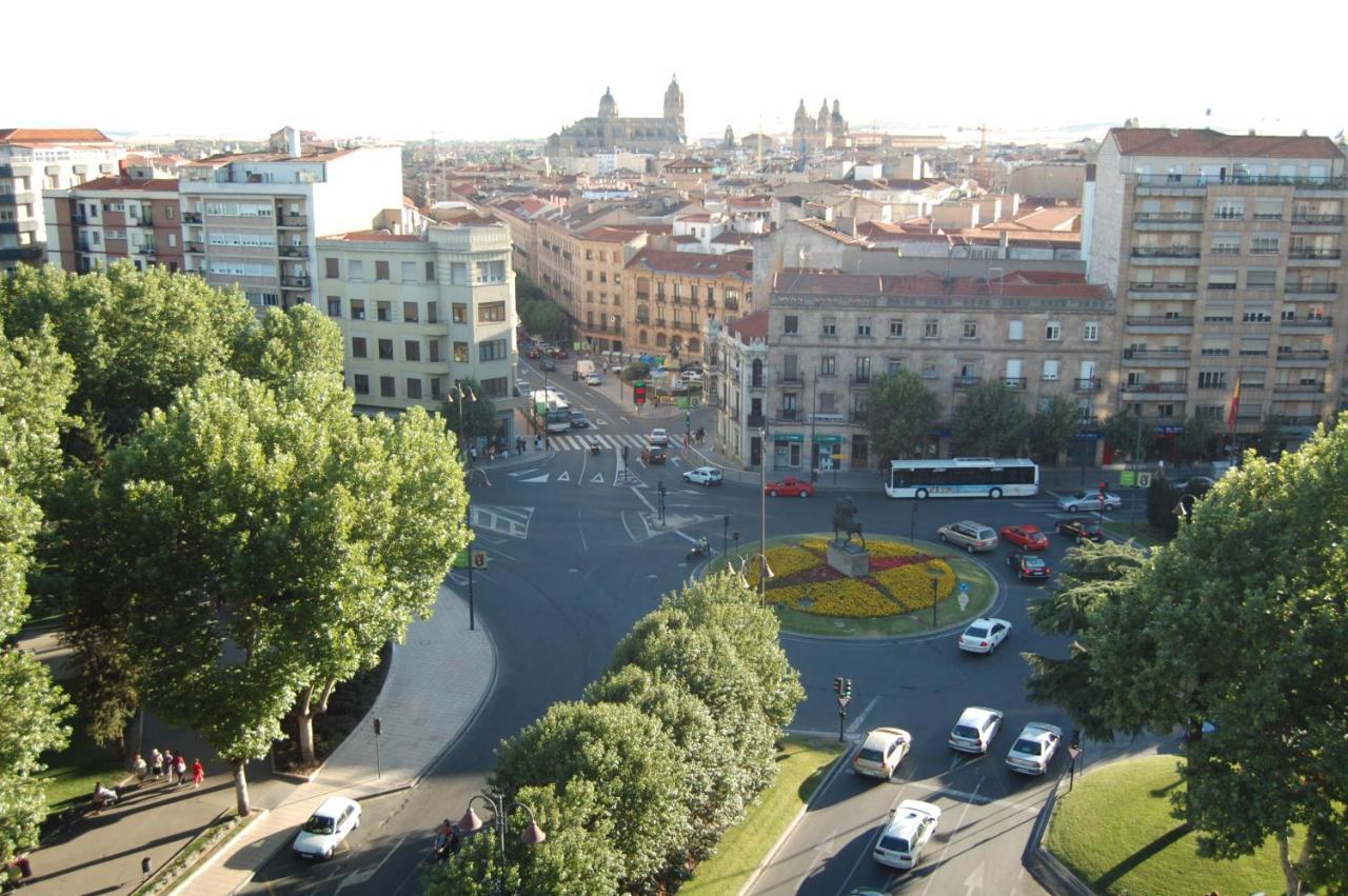 Hotel Alameda Palace Salamanka Exteriér fotografie The photo shows a city scene from an elevated perspective, possibly during the daytime. In the foreground, there is a roundabout with a circular flowerbed design in the center. Surrounding the roundabout, several vehicles are seen moving through the 